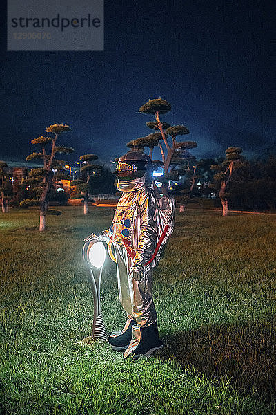Spaceman standing at a lamp in a park at night