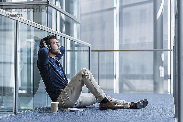 Businessman with headphones sitting on the floor relaxing