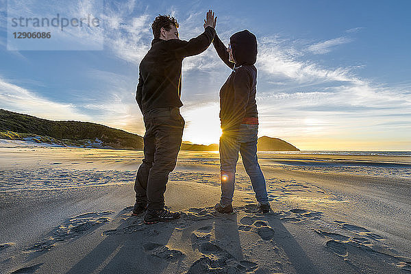 New Zealand  South Island  Puponga  Wharariki Beach  Couple high fiving on the beach at sunset