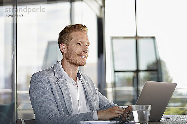 Smiling businessman with laptop on desk in office