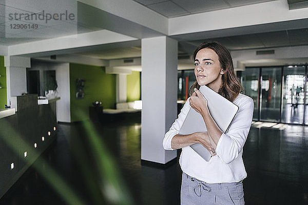 Businesswoman standing in office  holding laptop