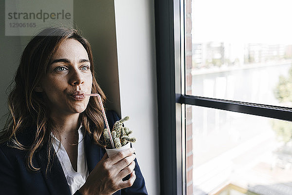 Businesswoman drinking from a straw  sticking in a cactus pot