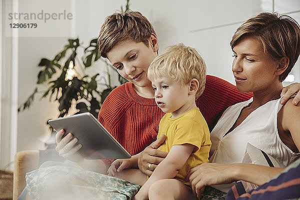 Two mothers looking at a tablet computer with their child at home