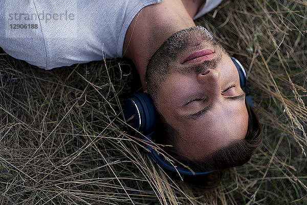 Relaxed man lying in field listening to music with headphones