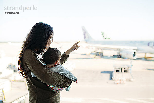 Mother holding a baby girl at the airport  pointing at the airplanes