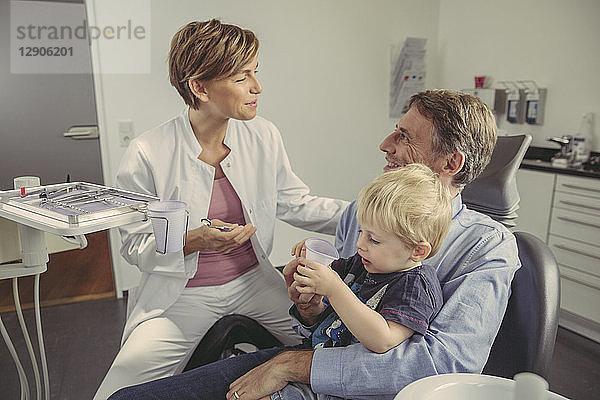 Female dentist talking to patient with son sitting on his lap
