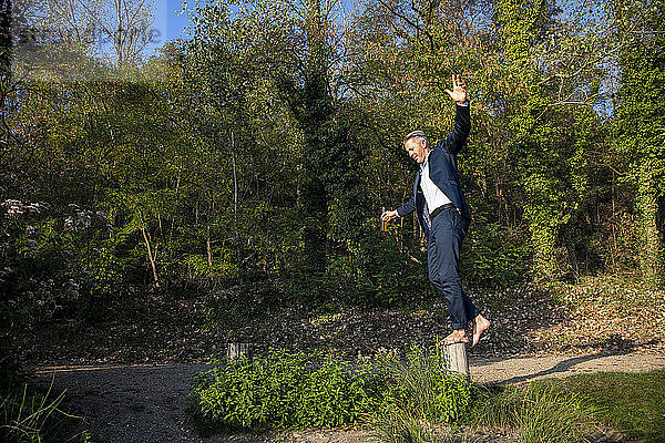 Businessman balancing barefoot on pole in nature