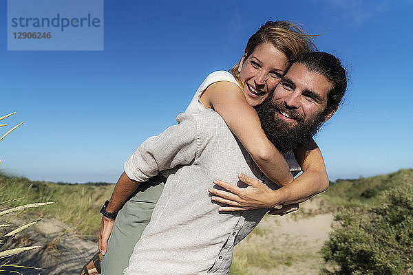 Young man carrying his girlfriend piggyback in the dunes