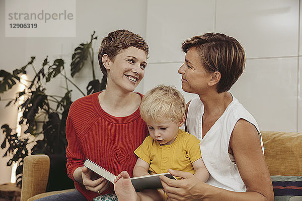 Two mothers reading a book with their child at home