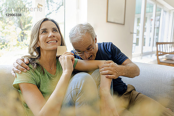 Playful mature man biting in woman's arm holding credit card at home
