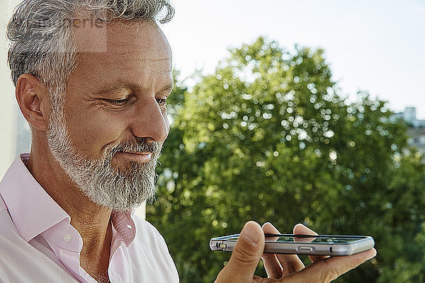 Portrait of smiling mature man holding smartphone outdoors