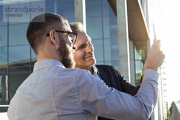 Two businessmen sharing a tablet outdoors