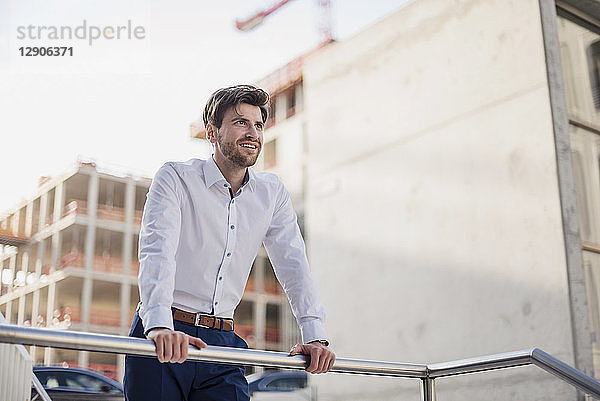 Portrait of smiling businessman in the city leaning on railing