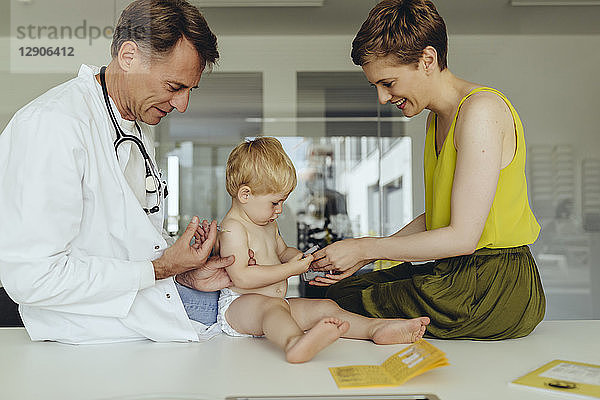 Pediatrician vaccinating toddler  injecting infant's arm  mother watching
