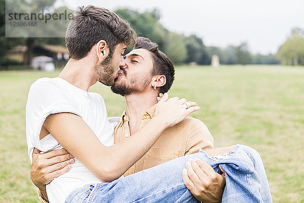Kissing young gay couple in a park