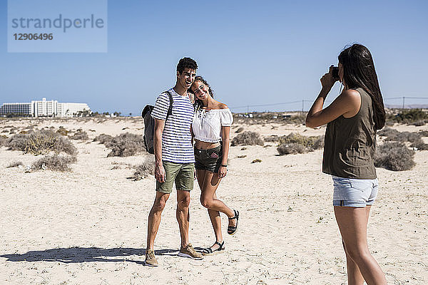 Young woman taking pictures of a young couple on the beach