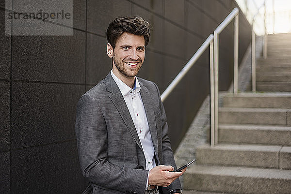 Portrait of smiling businessman with cell phone on stairs