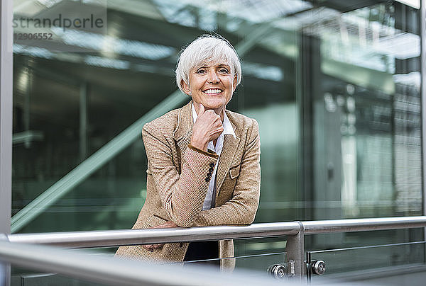 Portrait of smiling senior businesswoman leaning on railing in the city