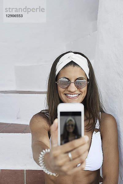 Portrait of smiling young woman wearing white bikini taking selfie with smartphone