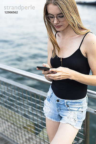Young woman standing at East River  using smartphone