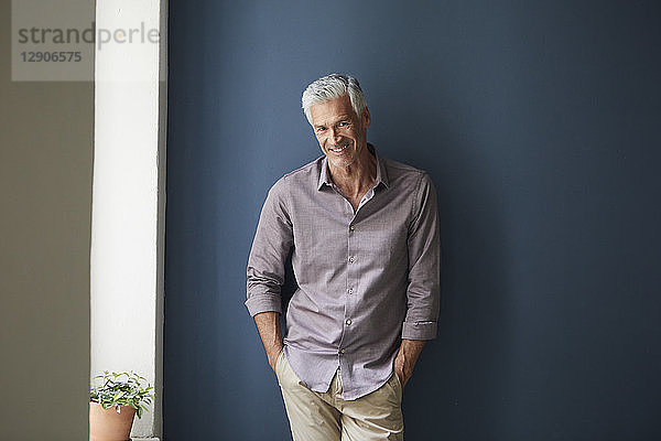 Portrait of confident mature man at home leaning against blue wall
