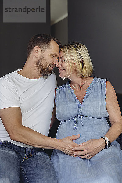 Mature man and his pregnant mature wife sitting on bed touching her belly