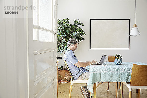 Mature man at home sitting at table  using laptop