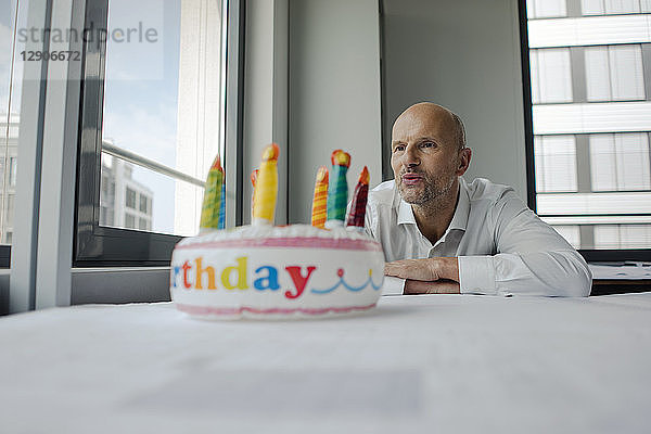 Businessman celebrating his birthday in the office  blowing out candles