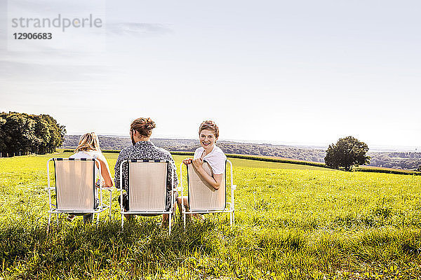 Friends sitting on camping chairs in rural landscape
