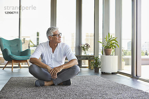 Mature man sitting on carpet at home looking out of window