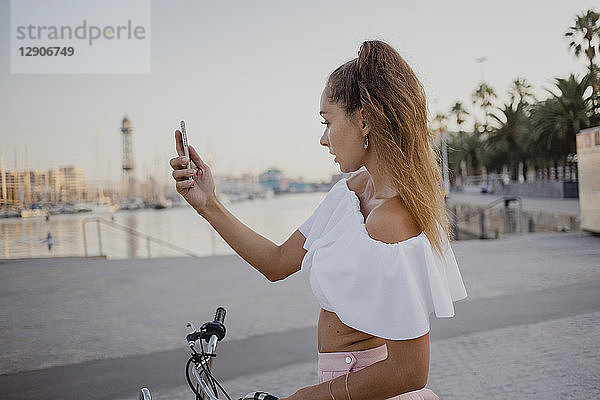 Fashionable young woman exploring Barcelona with a bicycle  using smartphone