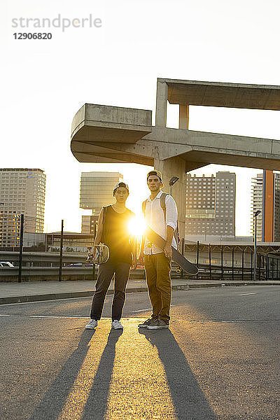 Portrait of two young men with skateboards in the city at sunset