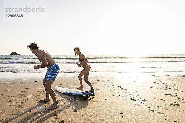 Young man showing young woman how to surf on the beach