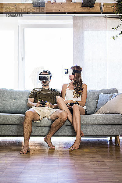 Couple sitting on couch at home wearing VR glasses playing video game