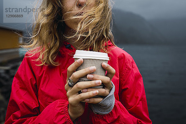 Norway  Lofoten  close-up of young woman at the coast holding takeaway coffee
