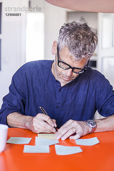 Mature man writing notepads on table at home
