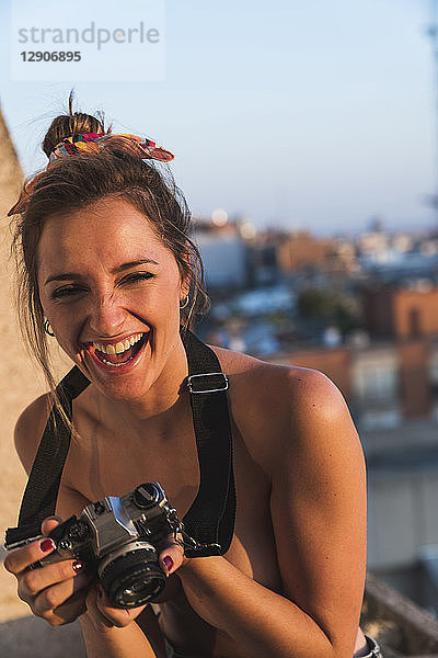 Laughing topless young woman with camera on balcony