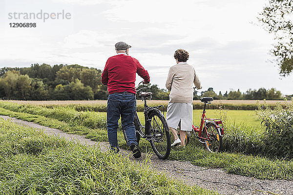 Senior couple pushing bicycles in rural landscape