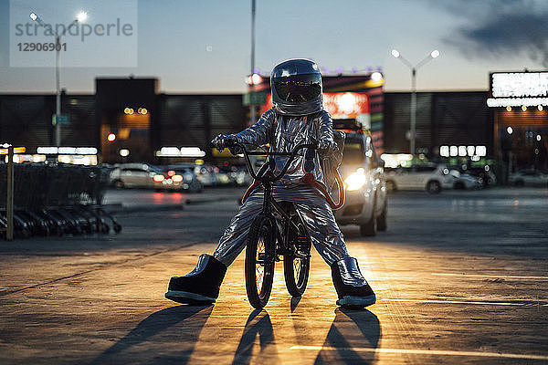 Spaceman in the city at night on parking lot with bmx bike