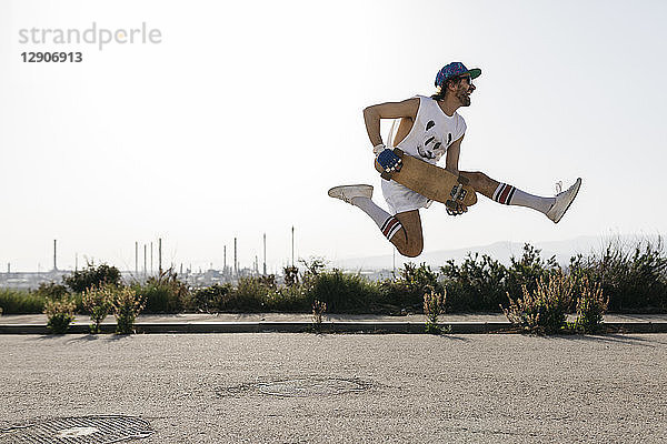 Sportive man jumping above ground with skateboard on hands