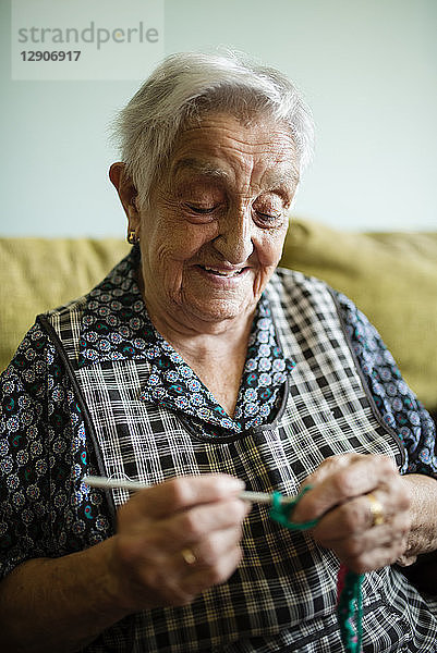 Portrait of smiling senior woman crocheting on the couch at home