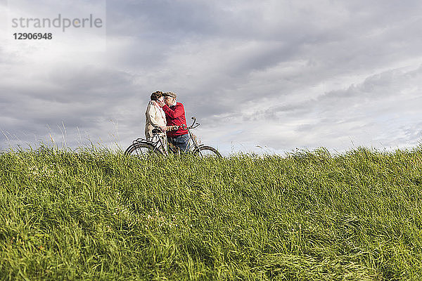 Senior couple with bicycles kissing in rural landscape under cloudy sky