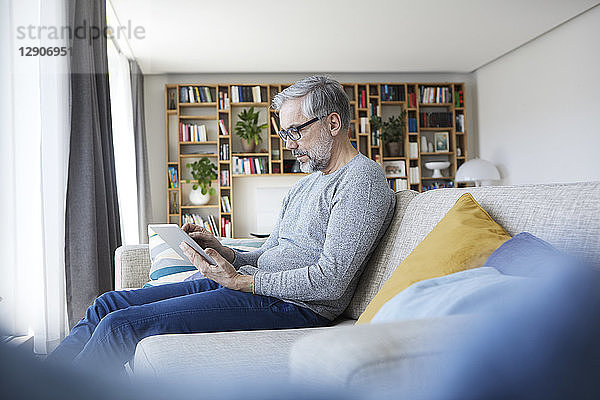 Mature man sitting on couch at his living room using tablet