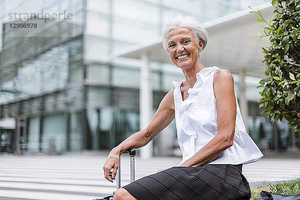 Portrait of happy senior woman with baggage sitting in the city