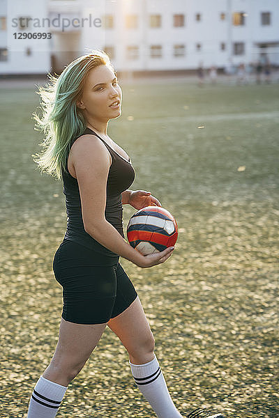 Young woman walking on football ground holding the ball