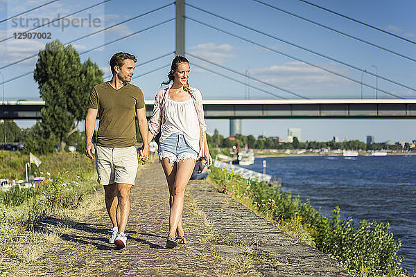 Happy couple walking hand in hand on waterfront promenade in summer