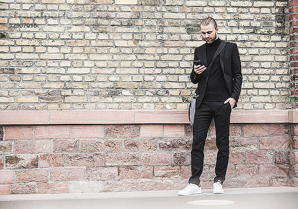 Young man standing at brick wall looking at cell phone