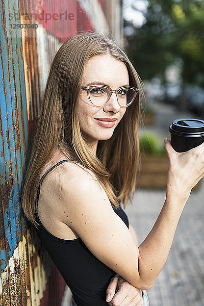 Young woman holding cup of coffee  standing in front of metal fence with stars and stripes