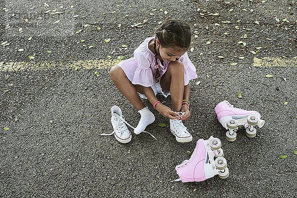 Little girl wearing pink blouse and braids tying shoes after roller skating