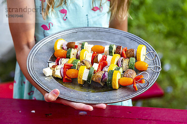 Girl holding plate with vegetarian grill skewers  tomato  yellow and green zucchini  tofu  feta  onion and champignon